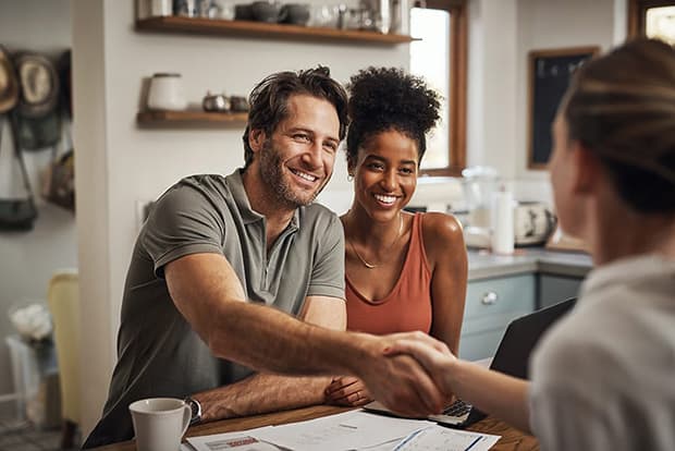 Couple meeting with a business woman going over paperwork at a desk.