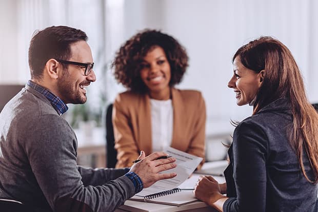 3 business people sitting at a table talking and looking at paperwork.