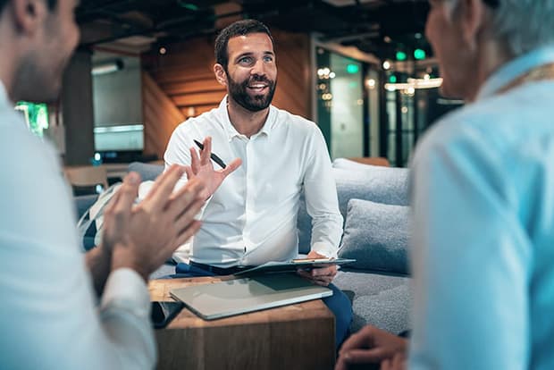 3 business men talking sitting on couches in a lobby.