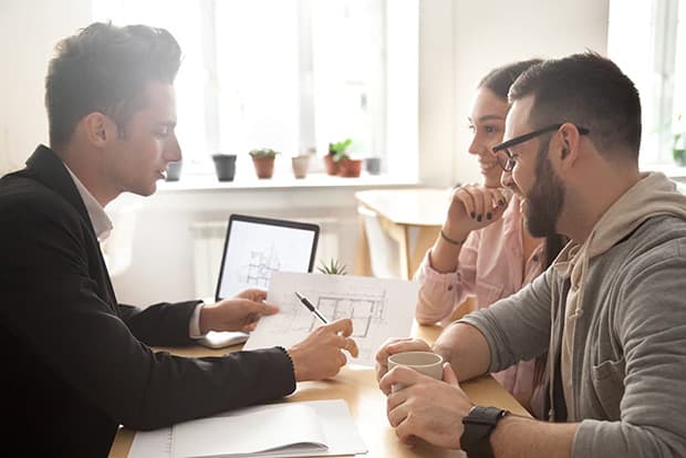 Couple meeting with a business man going over paperwork at a desk.