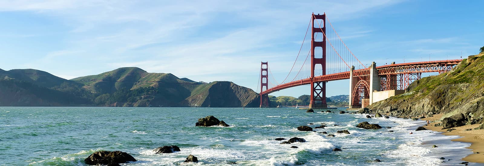 Aerial view of the San Francisco Golden Gate Bridge with blue water and mountains in the background.
