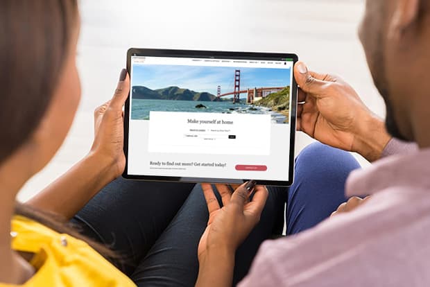 Back of a couple looking at an iPad with the Corcoran Global Living website on it.