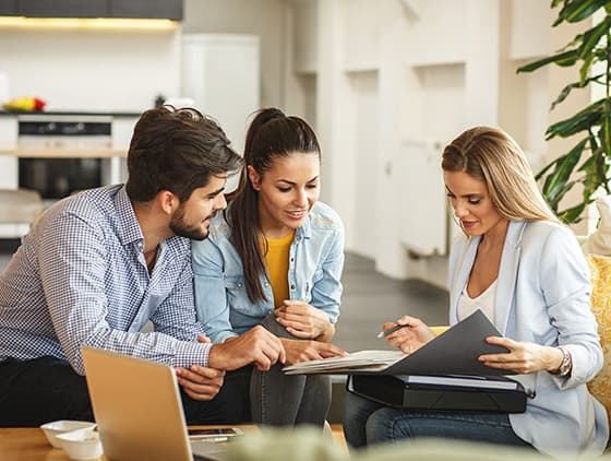 2 women and 1 man sitting on a couch looking a presentation with a laptop open.
