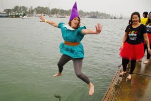 Person dressed in an elf costume with a purple pointy hat jumping into the lake with arms widespread.