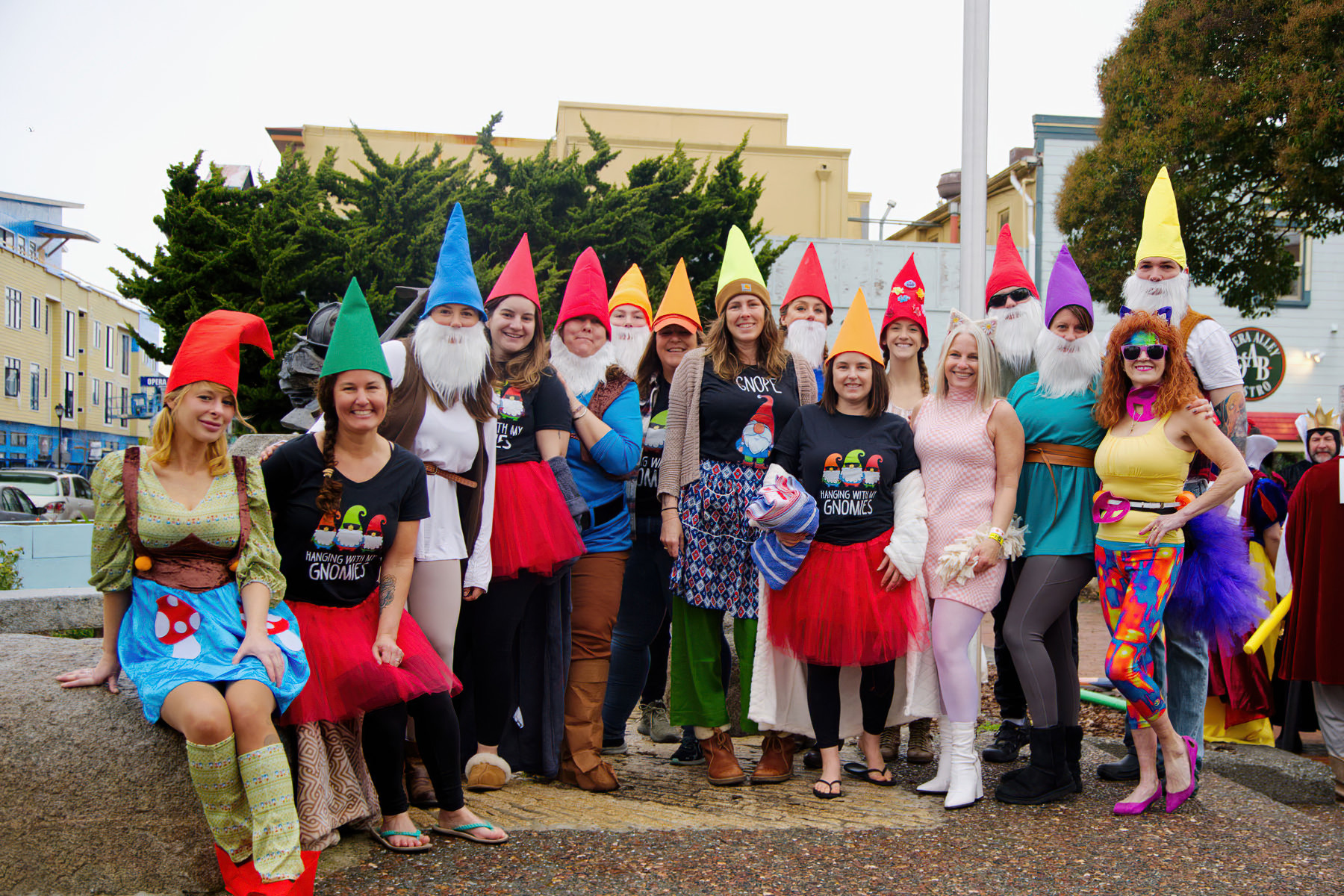 A group of people dressed up as elves. They are smiling and posing for the photo in front of a shopping center on a rainy day.