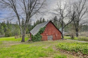 rustic red colored a-frame barn in the daytime set in a forest setting.