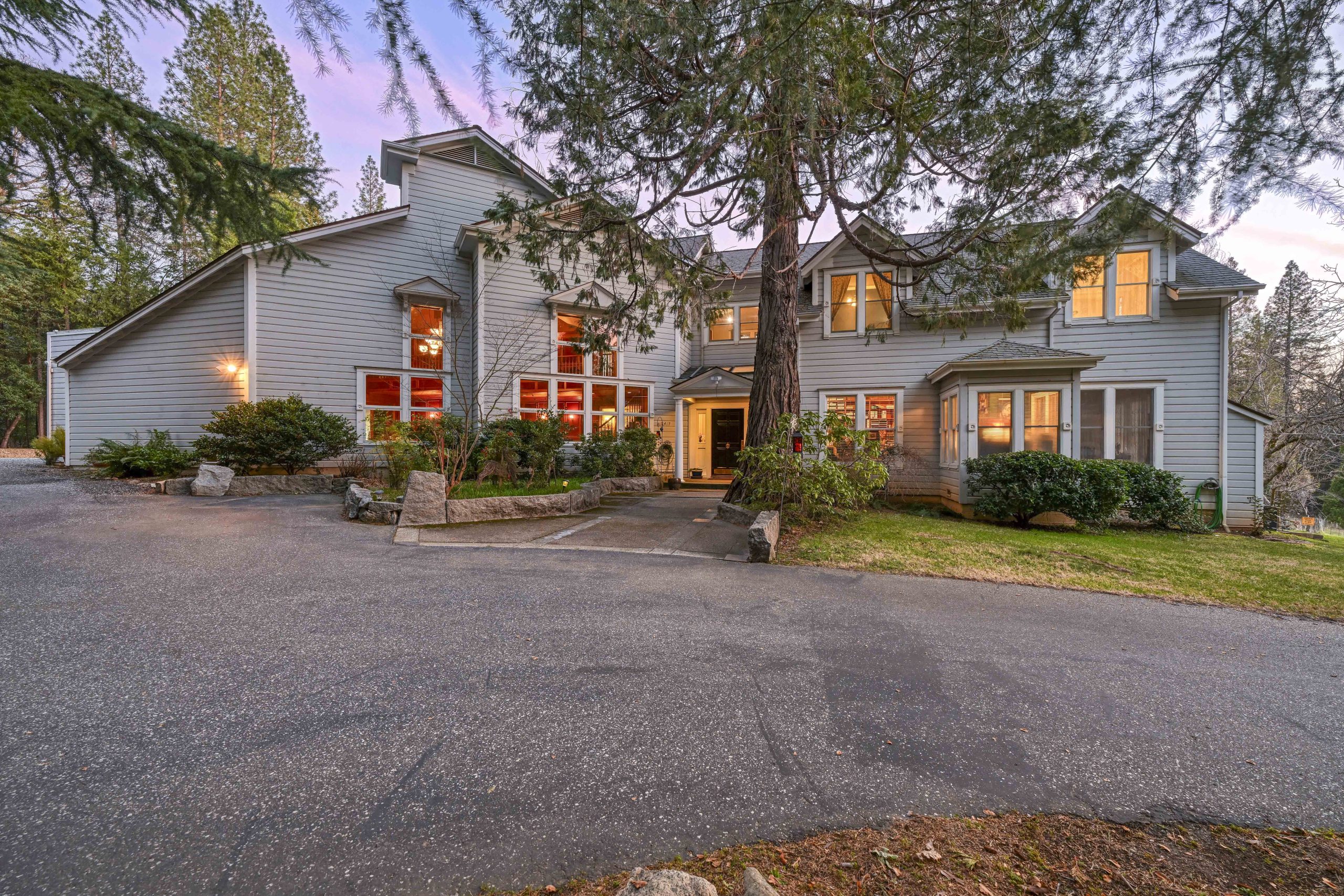 exterior of large gray home at dusk with lights on in a forest setting.